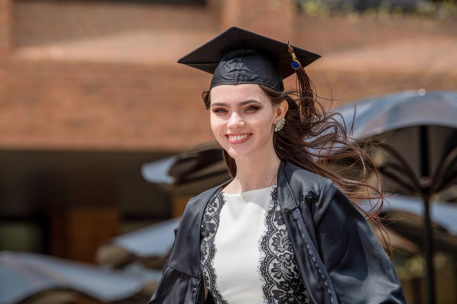 A graduating Kent State University student smiles in her cap and gown at Risman Plaza in spring 2020.