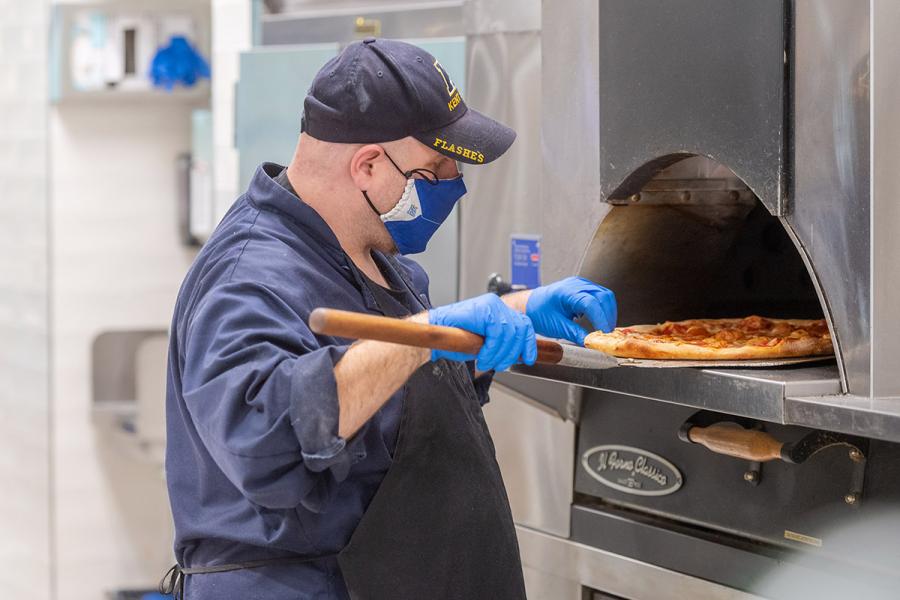 A Kent State employee loads a pizza into the oven. 