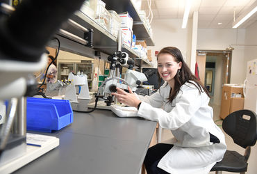 Photo of Ya'el Courtney in a lab coat, conducting research