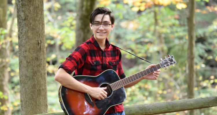 Honors College student Daniel Zalamea poses for a photo with his guitar in the woods.