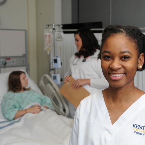A Kent State nursing student poses as another nursing student cares for a patient in the background
