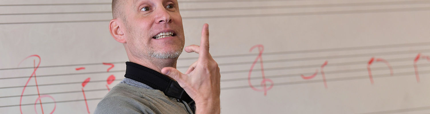 Music instructor in front of a white board with staff and musical notes written on it