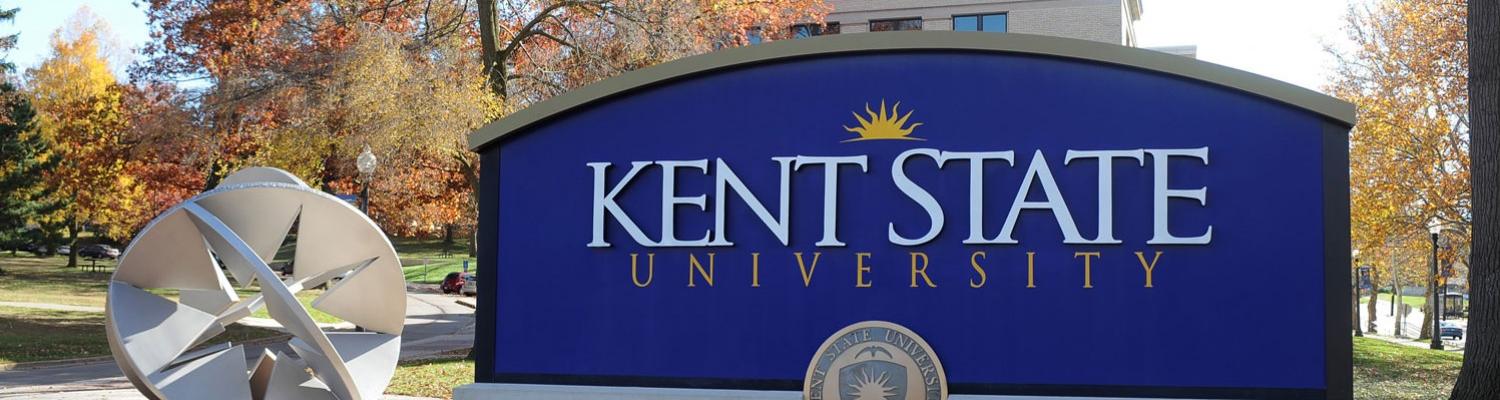 A large blue Kent State University sign on display on a bright fall day.
