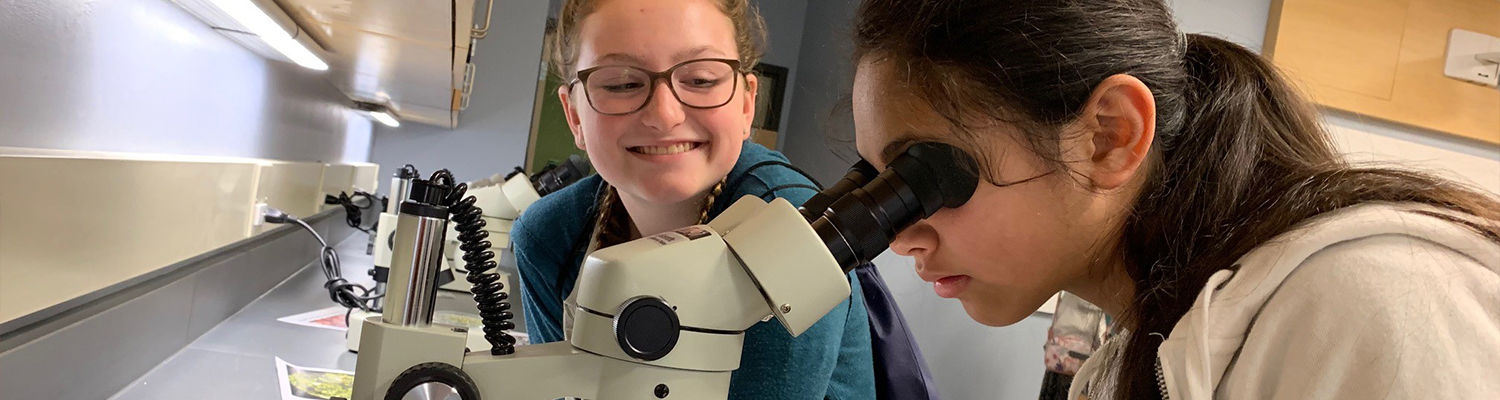 Young students looking into microscope and smiling