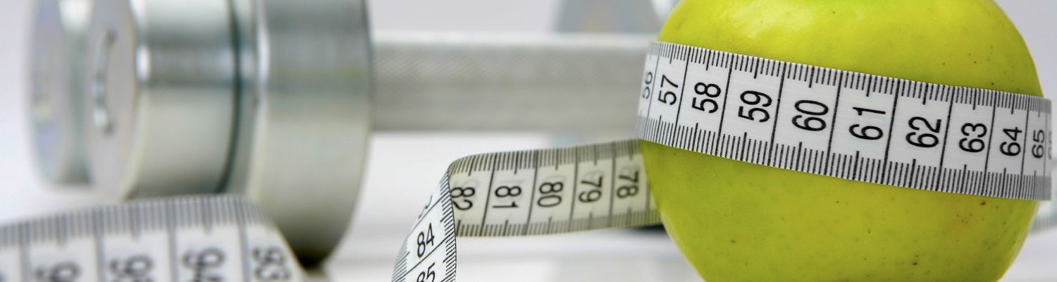 A pair of dumbbells sit behind an apple, which is wrapped in measuring tape