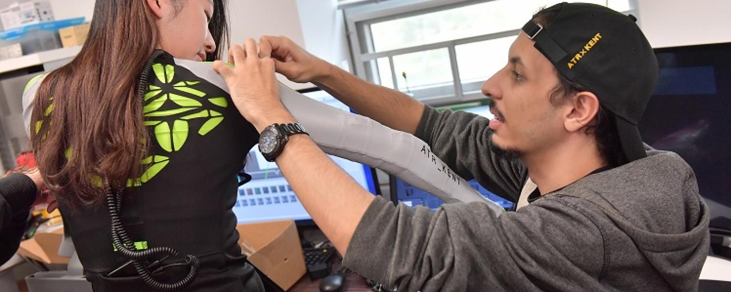Student adjusting arm of programmable jacket worn by another student