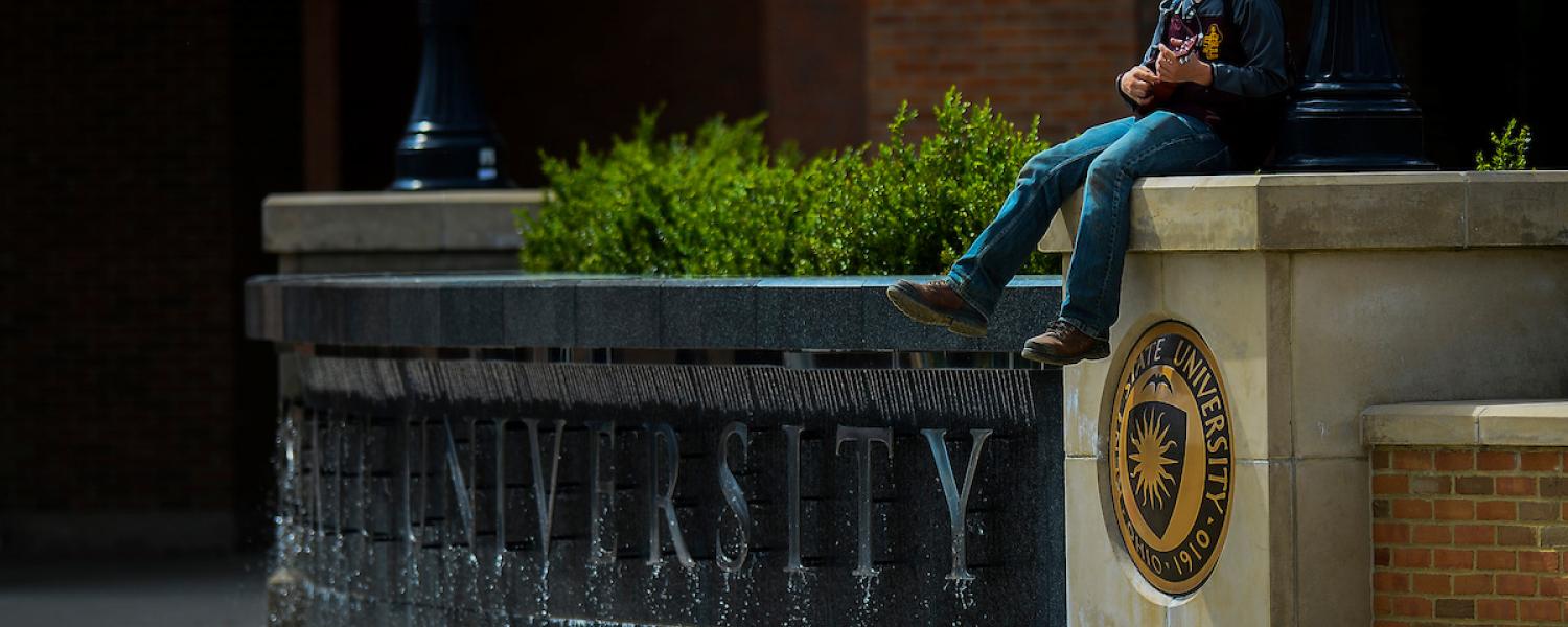Student sits on Risman Plaza above the fountain playing the guitar.