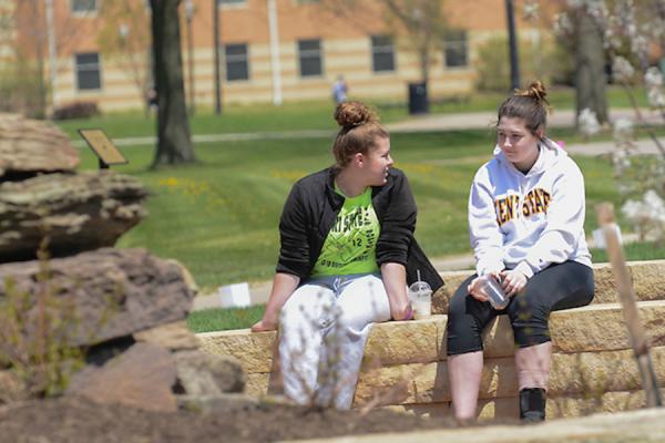 2 students sitting on campus by a fountain, with centennials and eastway center in the background