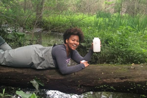 Student laying on log with water sample over creek