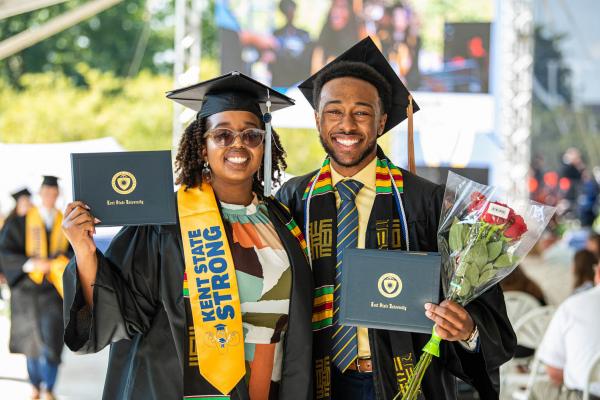 New Kent State graduates smile while holding their degrees after their commencement ceremony in August 2021.