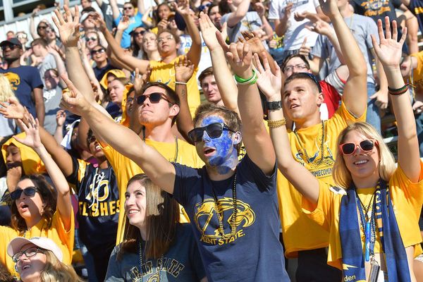 Kent State alumni and students, wearing blue and gold gear, holding their hands up in the air