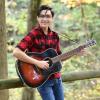 Honors College student Daniel Zalamea poses for a photo with his guitar in the woods.