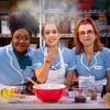 picture of the three leading stars from National Tour of Waitress wearing uniforms behind a table of baking supplies